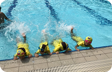 Children practicing kicking water along pool edge