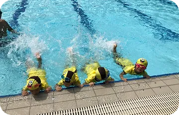 Children practicing kicking water along pool edge