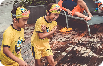 Kids in yellow swim suits smiling and walking on poolside deck