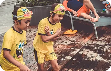 Kids in yellow swim suits smiling and walking on poolside deck