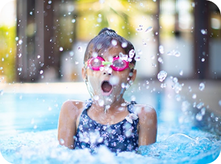 Happy child with goggles splashing in swimming pool