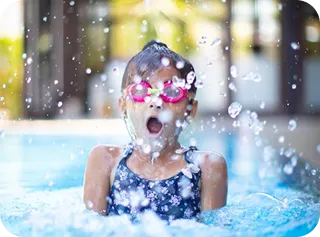 Happy child with goggles splashing in swimming pool